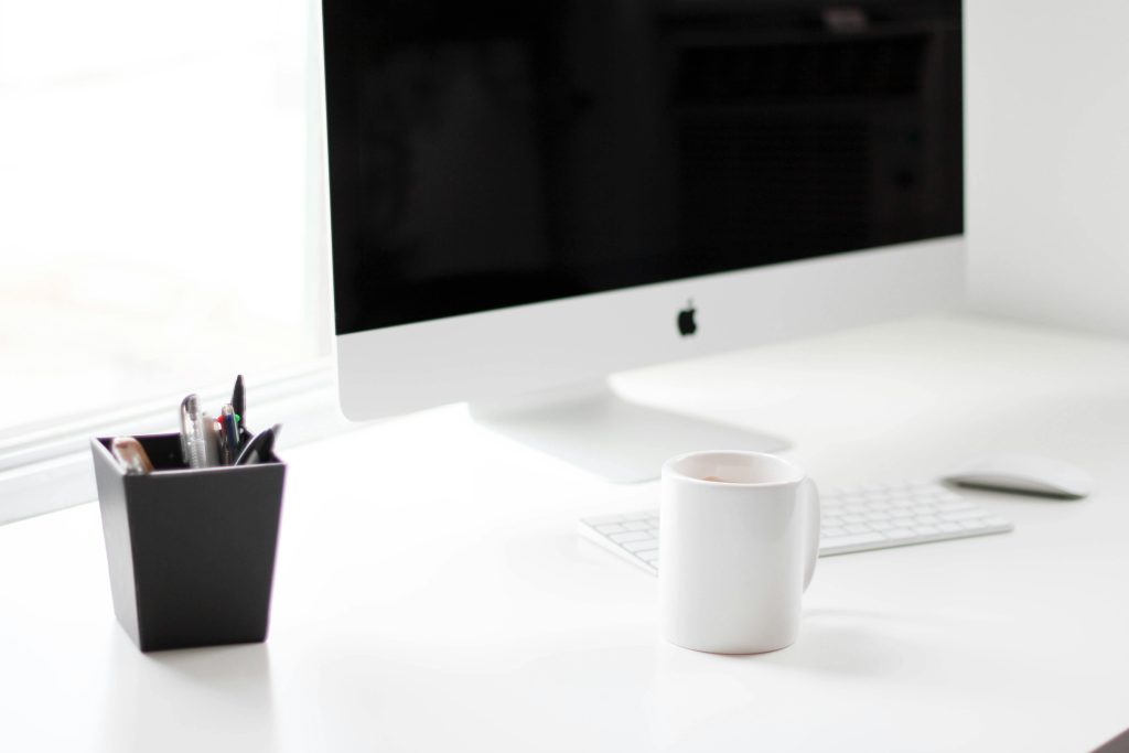 A minimalist work desk featuring a desktop computer, coffee mug, and office supplies.